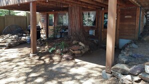Una terraza de madera con un tronco de árbol rústico, un porche cubierto y un patio trasero cercado.