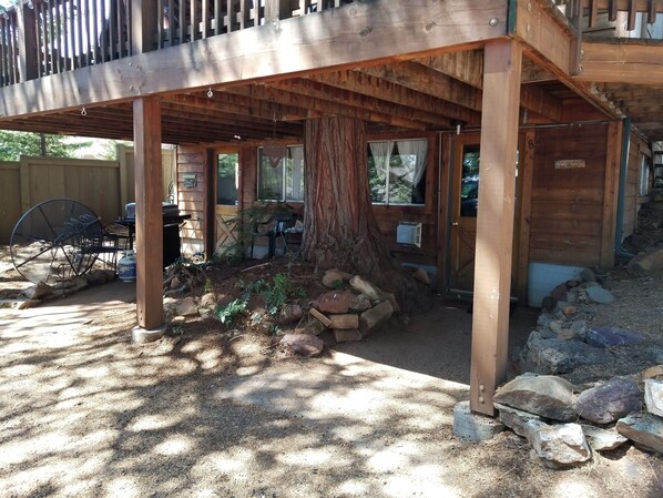 Una terraza de madera con un tronco de árbol rústico, un porche cubierto y un patio trasero cercado.