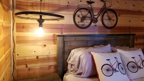 Una habitación de madera con una cama, una bicicleta como adorno en la pared y una lámpara colgante.