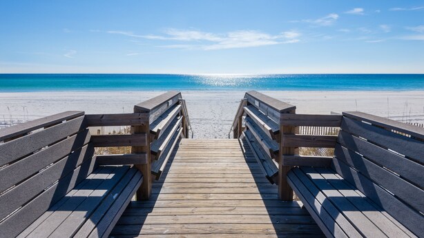Une promenade en bois qui mène à une plage, avec un ciel bleu dégagé.