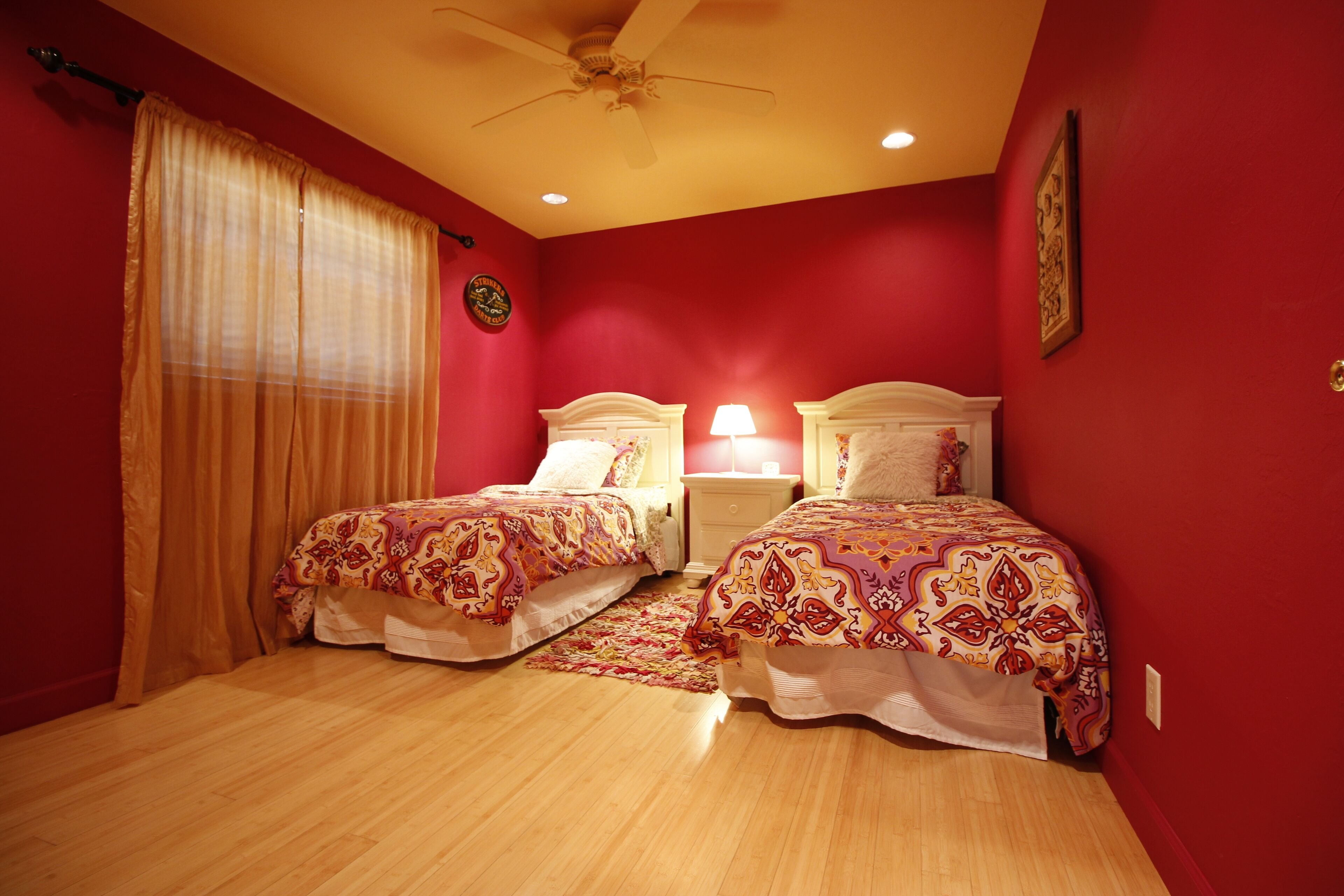 A bedroom with two beds, wooden flooring, a ceiling fan, and red walls.