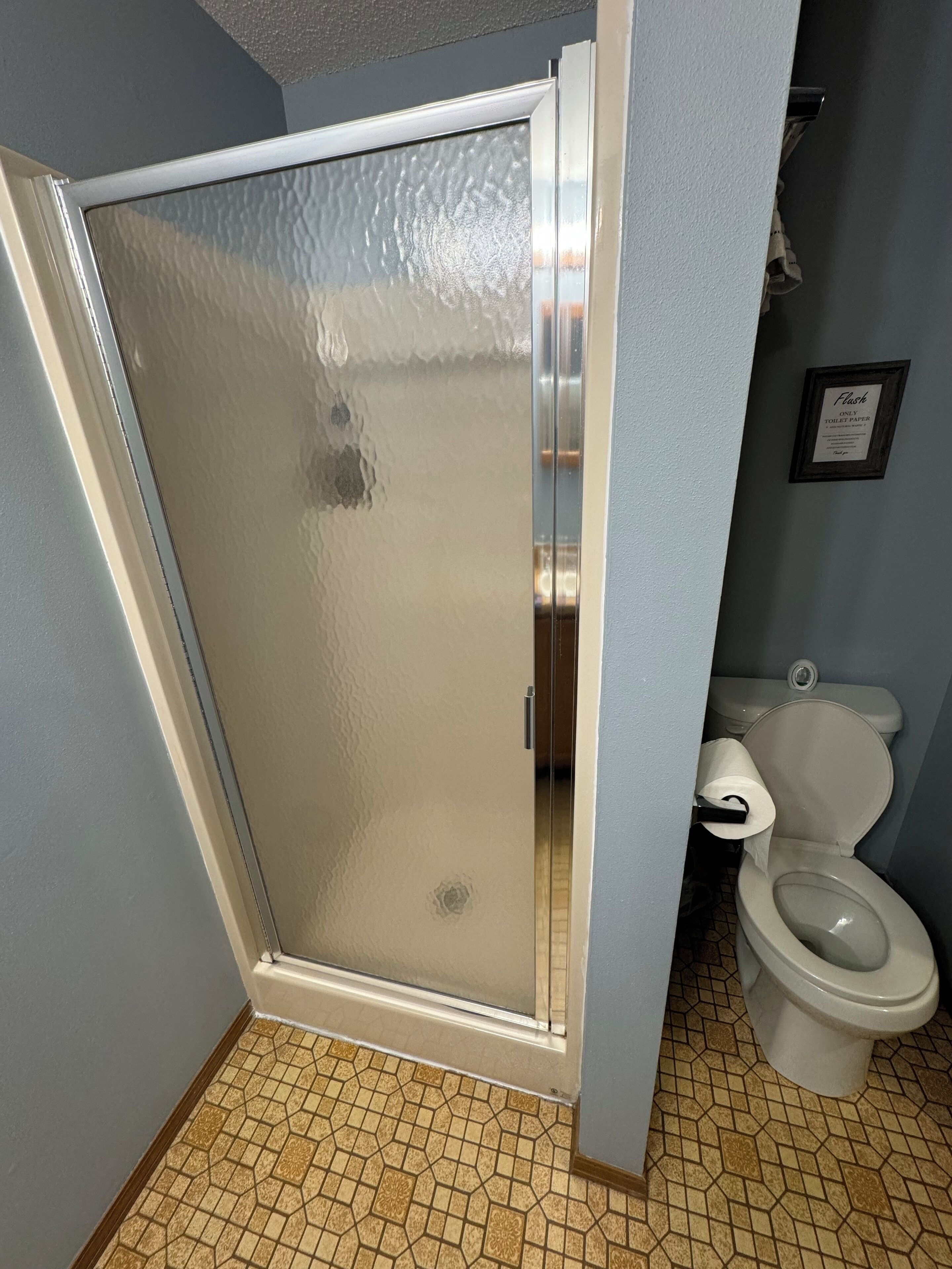 Ein Badezimmer mit Duschabtrennung, Toilette und einem Schild, das die Nutzung von Toilettenpapier anweist.