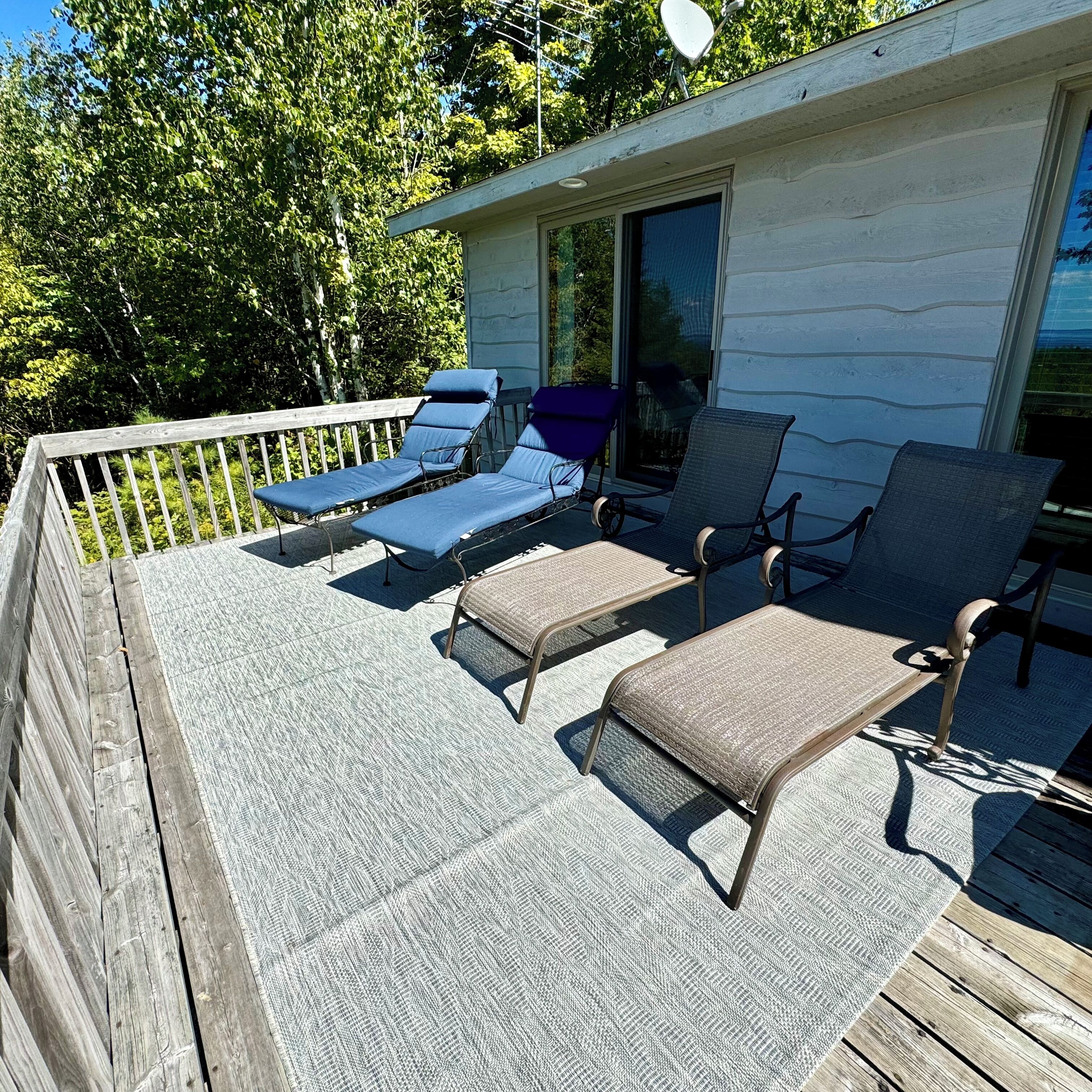 A covered deck with lounge chairs and a small building with a sliding glass door.