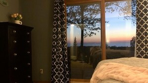 Un dormitorio con cama, cómoda y vista a un atardecer a través de una puerta de cristal.