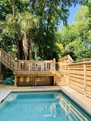 Une terrasse en bois avec une piscine, entourée d’arbres.