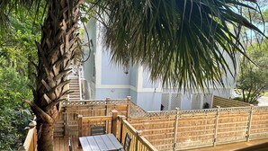 Una terrassa de fusta amb taula i cadires, envoltada per una tanca de fusta i un arbre gran.