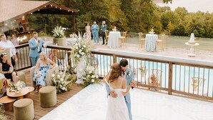 Une cérémonie de mariage sur une terrasse en bois, avec vue sur un lac, entourée d’invités et décorée de fleurs.