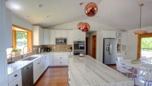 Une cuisine moderne avec des meubles blancs, un îlot en marbre, des appareils en acier inoxydable et des luminaires suspendus.