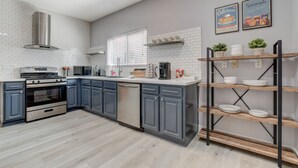 A modern kitchen with grey cabinets, stainless steel appliances, and a wooden shelf with dishes. - Chic Single Story 3br House Close To Strip & Airport (Las Vegas)