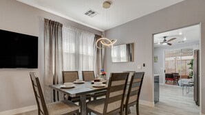 A modern dining area with a wooden table and chairs, a flat-screen TV mounted on the wall, and a ceiling fan. - Chic Single Story 3br House Close To Strip & Airport (Las Vegas)