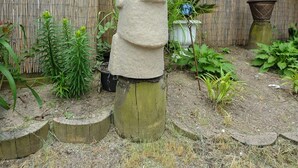 Escultura de cabeza de piedra en un jardín con valla de bambú, plantas en macetas y una decoración de pájaro azul.