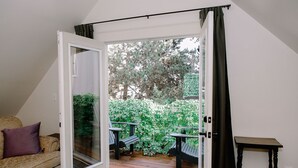 Puerta corredera abierta que da a un patio con terraza de madera, sofá y mesa.