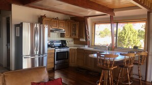 A modern kitchen with stainless steel appliances, wooden cabinets, and a large window providing a view of trees. - A Grandview over Capitol Reef National Park (Torrey)
