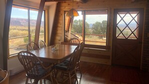 A dining area with a wooden table and chairs, large windows with a view of the landscape, and a wooden ceiling. - A Grandview over Capitol Reef National Park (Torrey)