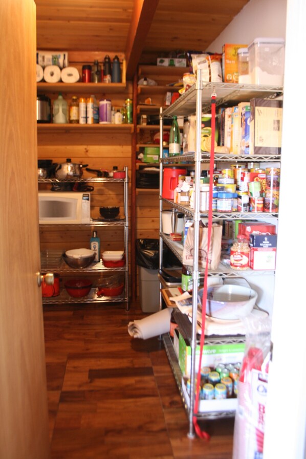 A narrow hallway with wooden flooring leading to a kitchen area with shelves stocked with various food items and kitchenware. - A Grandview over Capitol Reef National Park (Torrey)