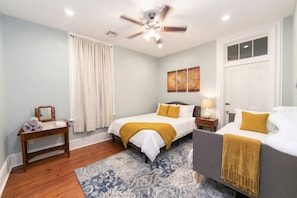 A bedroom with a bed, bedside tables, a mirror, a ceiling fan, and artwork on the wall. - Elysian Historic Cottage Historic Getaways (New Orleans)