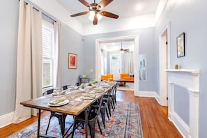 A dining area with a long table set for six, a ceiling fan, and a patterned rug.