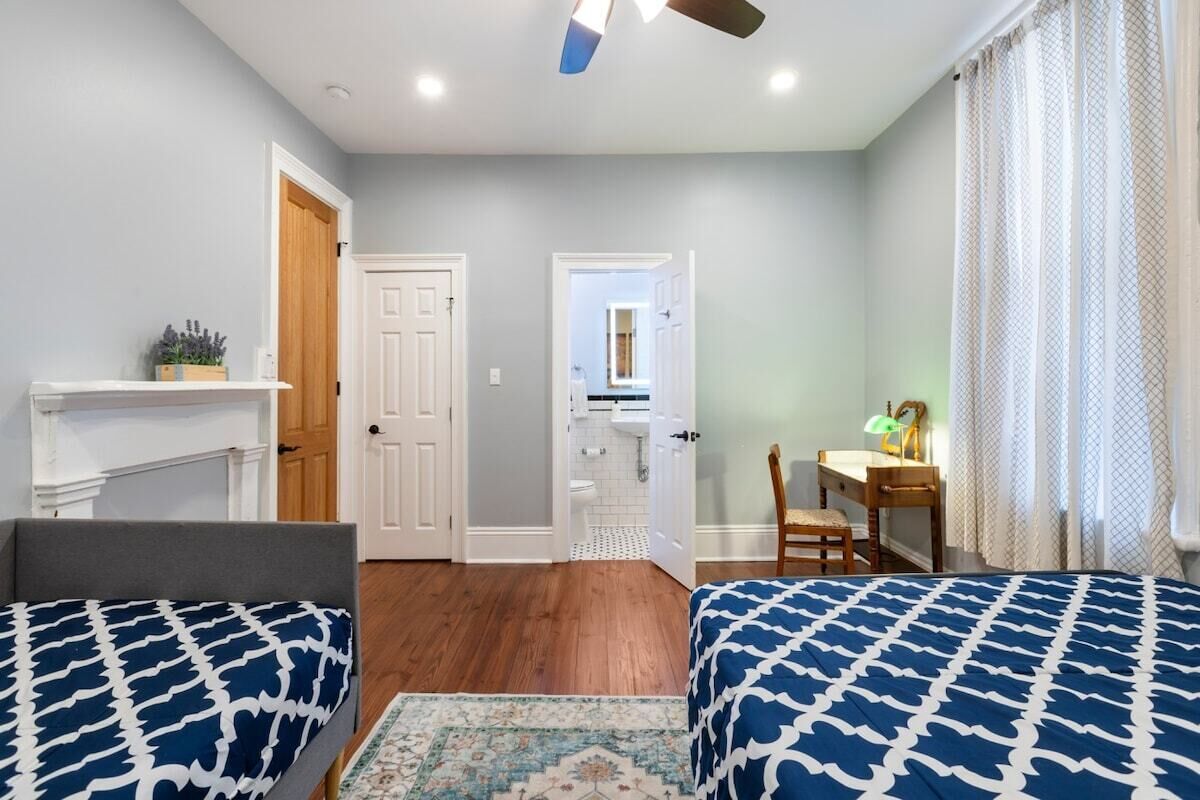 A bedroom with two beds, a desk, a chair, a mirror, and a door leading to a bathroom.