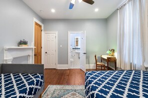 A bedroom with two beds, a desk, a chair, a mirror, and a door leading to a bathroom. - Michou's Marigny Historic Gem | Historic Getaways (New Orleans)
