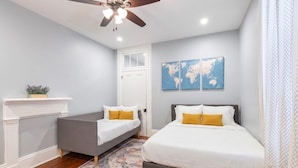 A bedroom with two beds, a ceiling fan, a world map on the wall, and a fireplace. - Michou's Marigny Historic Gem | Historic Getaways (New Orleans)