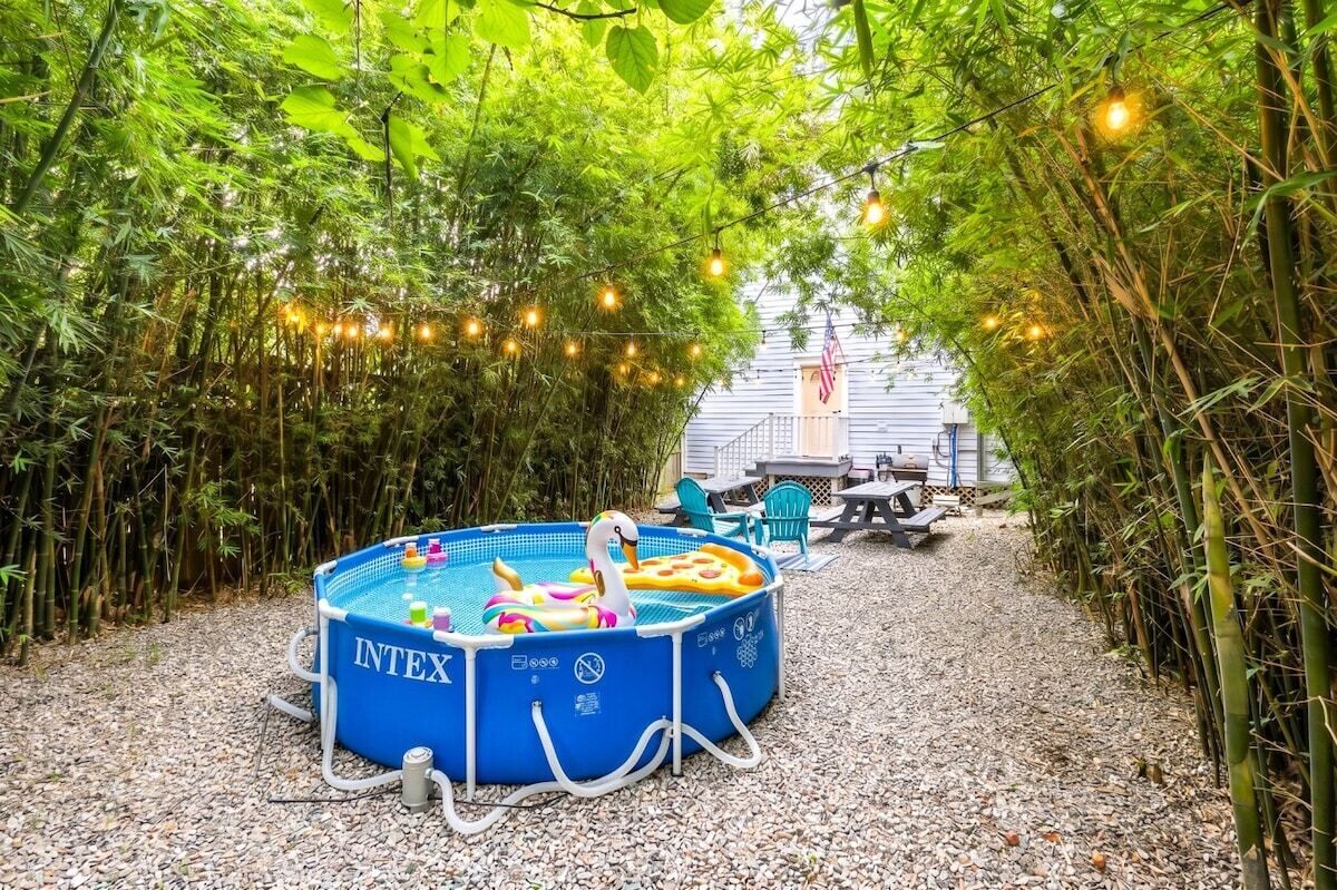 Ein blauer aufblasbarer Pool mit aufblasbaren Spielzeugen, umgeben von einem Bambuszaun und Lichterketten, mit einer Terrasse im Hintergrund.