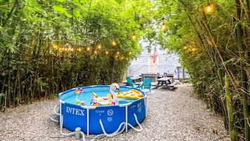 A blue inflatable pool with inflatable toys, surrounded by a bamboo fence and string lights, with a patio area in the background.