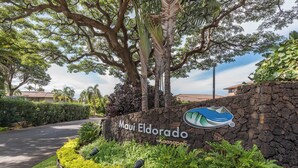 Segnale per 'Maui Eldorado Kaanapali' con un logo, immerso in una vegetazione rigogliosa e delimitato da un muro in pietra.