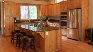 A kitchen with wooden cabinets, a stainless steel refrigerator, and a central island with stools. - Newer Built ski to ski lift , Extra Master Bedroom ,Sleeps 10 (Homewood)
