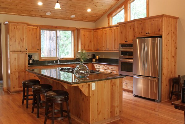 A kitchen with wooden cabinets, a stainless steel refrigerator, and a central island with stools.