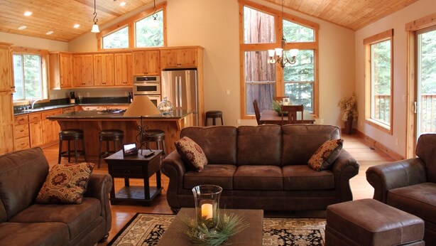 A spacious living area with a brown leather sofa, a coffee table with a candle, and a kitchen with wooden cabinets and a stainless steel refrigerator. - Newer Built ski to ski lift , Extra Master Bedroom ,Sleeps 10 (Homewood)
