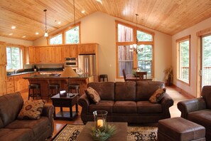 A spacious living area with a brown leather sofa, a coffee table with a candle, and a kitchen with wooden cabinets and a stainless steel refrigerator.