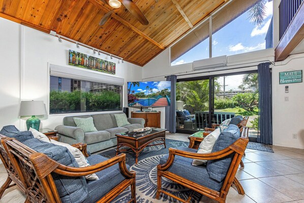 A spacious living area with a wooden ceiling, large windows, and a view of a tropical landscape.