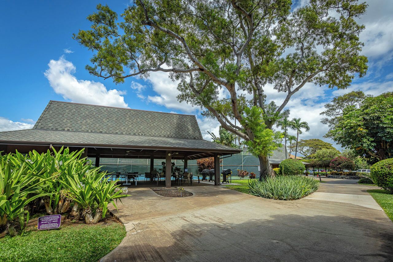 A building with a covered patio area, outdoor seating, and a large tree in the foreground.