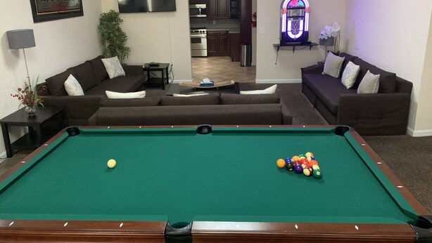 A living room with a pool table, two couches, a television, and a jukebox.
