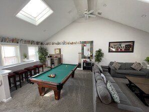 A living room with a pool table, a grey sofa, and a ceiling fan.