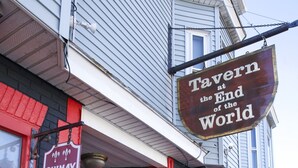 A building with a red door, a sign reading "Tavern at the End of the World," and a Guinness sign.