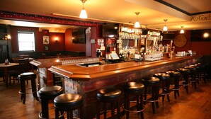 A bar with wooden stools, a bar counter, and a variety of bottles and glasses.