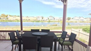 Un espacio al aire libre techado con una mesa y sillas, con vista a un cuerpo de agua y edificios a lo lejos.