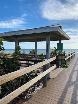 A wooden boardwalk leading to a covered pavilion with a view of the ocean.
