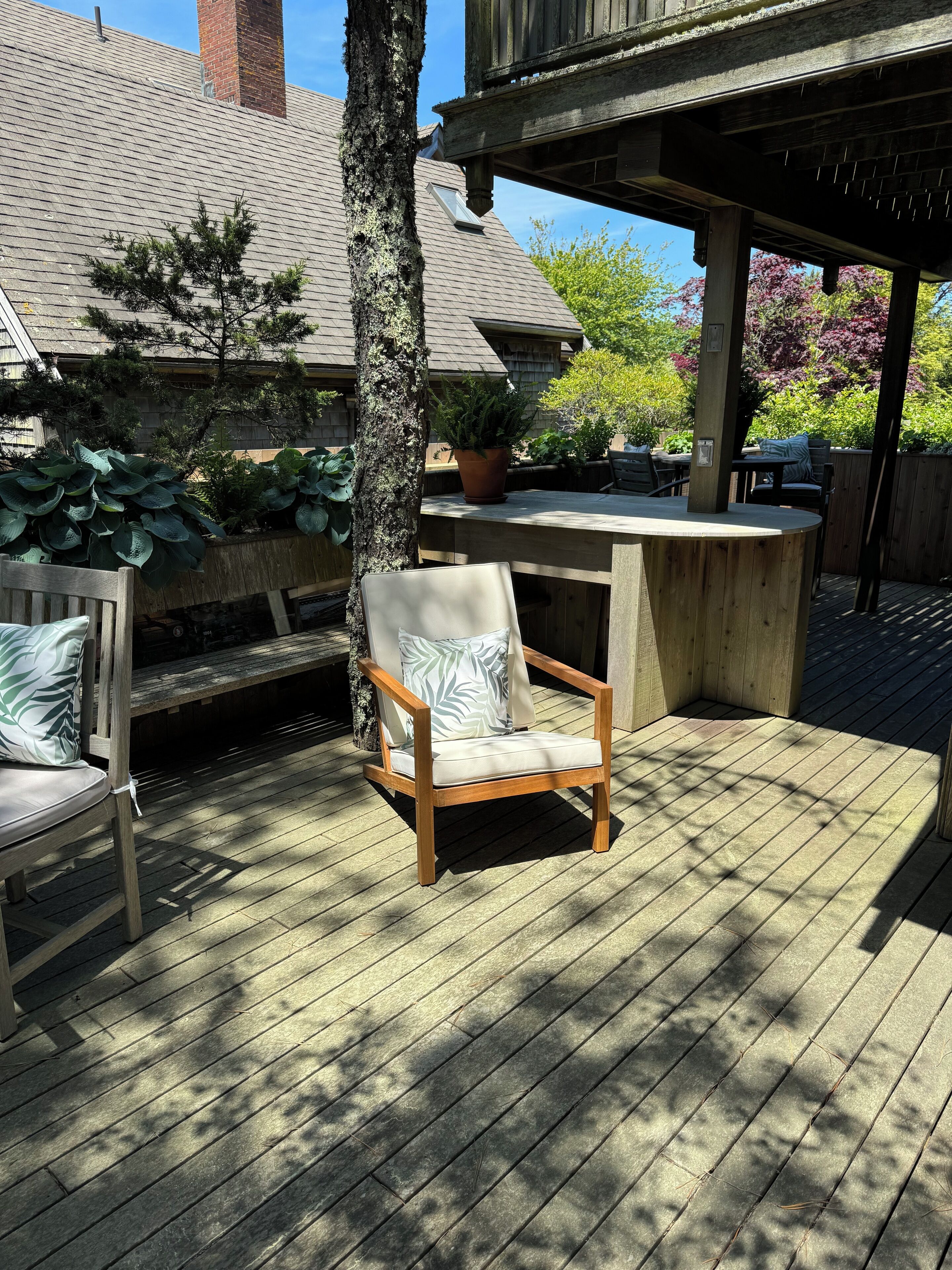 Een houten terras met een stoel en een tafel, omgeven door potplanten en een houten omheining.