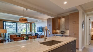 A modern kitchen with a large island, built-in cabinets, and a dining area with a view. - Experience paradise at Kahana's beachfront 3-bedroom condo near Kaanapali Beach  (Lahaina)