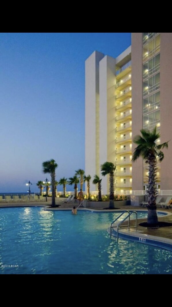 Guests can enjoy stunning views from the balconies overlooking the pool area with palm trees and lounge chairs.