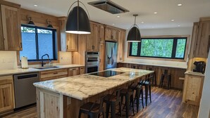 Una cocina moderna con armarios de madera, una isla de mármol, taburetes de bar y electrodomésticos integrados.