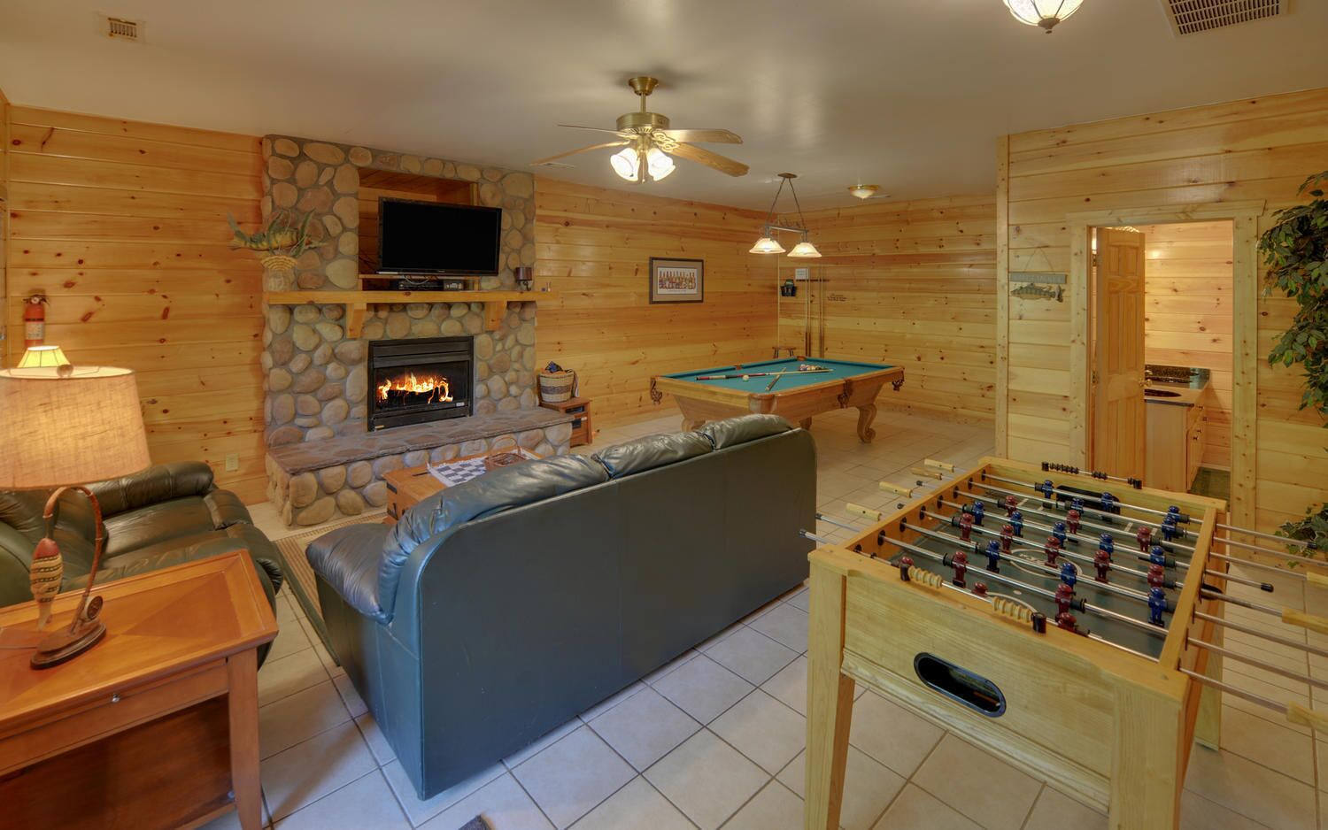 Una habitación acogedora con chimenea de piedra, mesa de billar, sofá y mesa de futbolín.