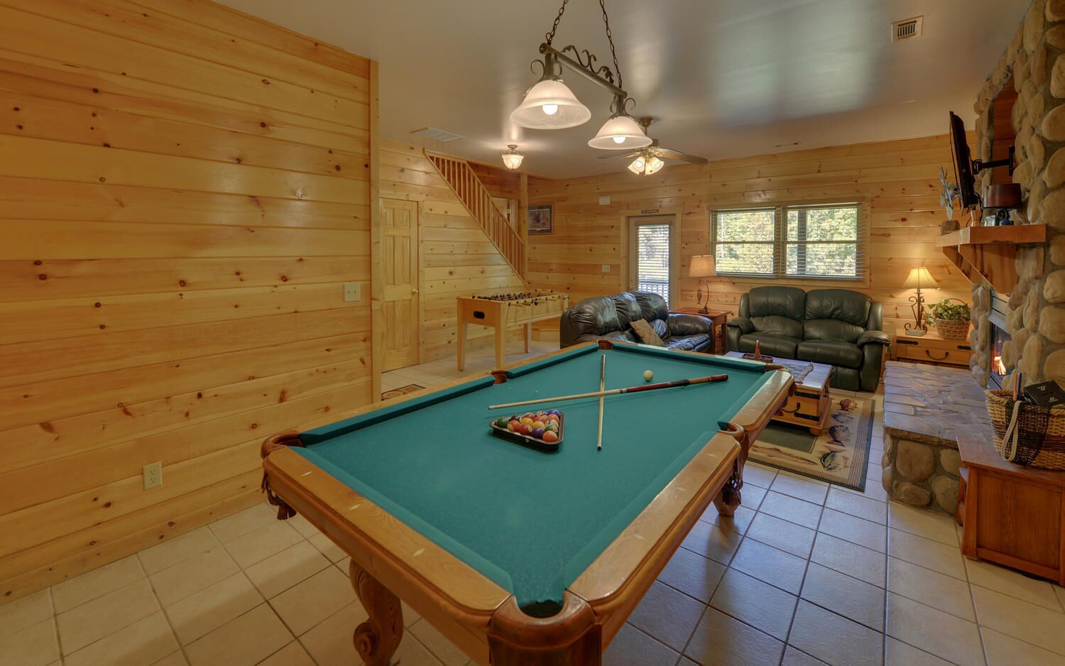A cozy cabin with a pool table, a leather sofa, and a fireplace.