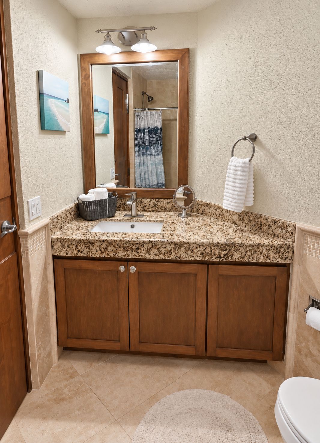 A bathroom with a granite countertop, wooden cabinets, a mirror, a towel rack, and a toilet.
