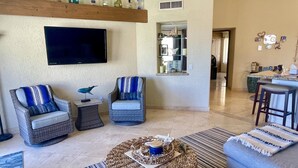 A living room with wicker furniture, a flat-screen TV, and a dining area with stools. - ALL NEW remodeled condo! Ocean Front on Beach 2 Bd 2 Ba Upper Level (Cabo San Lucas)