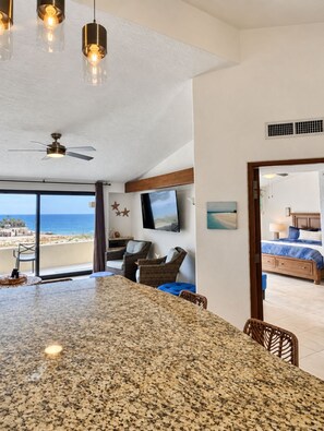 Een moderne hotelkamer met een groot granieten eiland, een flatscreen televisie, een plafondventilator en uitzicht op het strand.