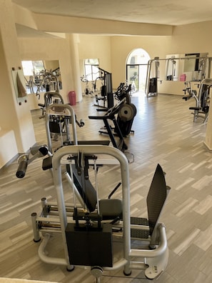 A spacious gym with various exercise machines, a large mirror, and a wooden floor. - ALL NEW remodeled condo! Ocean Front on Beach 2 Bd 2 Ba Upper Level (Cabo San Lucas)