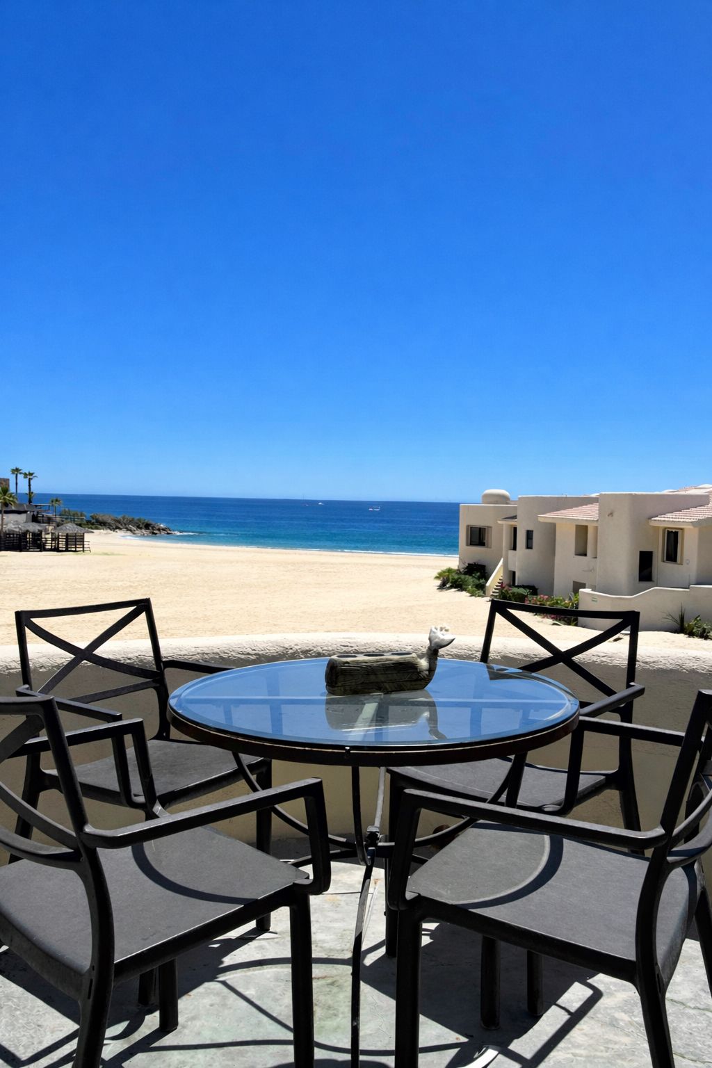A round glass table with four chairs, a stone sculpture, and a view of a beach and ocean.